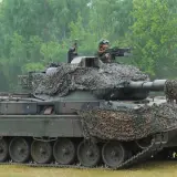 Ein Leopard 1 Panzer mit Tarnnetz und einem Soldaten am Maschinengewehr. Sein Gewicht ist beeindruckend.