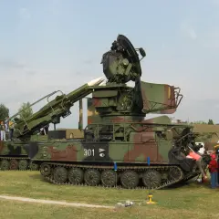 Ein Raketenwerfer SA-6 mit Raketen und Radar steht auf einem Feld. Kinder und Erwachsene betrachten die militärische Ausrüstung.