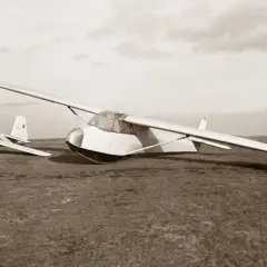 Ein Segelflugzeug vom Typ Musger MG 19 steht auf einer Wiese. Ein weiteres Flugzeug ist im Hintergrund zu sehen.