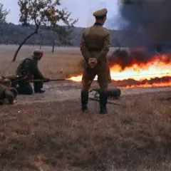 Soldaten im 2. Weltkrieg üben den Einsatz eines Flammenwerfers. Ein Mann zielt mit dem Gerät, während ein anderer auf dem Boden liegt.