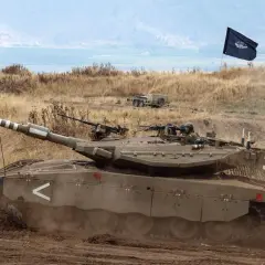 Ein Merkava Panzer fährt durch staubiges Gelände, begleitet von zwei Fahnen.