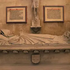 Das Michael Wittmann Grab zeigt eine liegende Steinfigur eines Bischofs mit gefalteten Händen. Tafeln mit Texten flankieren die Skulptur.