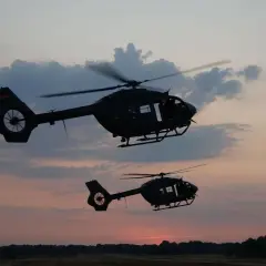 Zwei KSK Hubschrauber fliegen im Abendrot über eine Waldlandschaft.