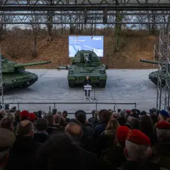 Drei Panzer, ein Redner und eine Zuschauermenge bei einer Veranstaltung.