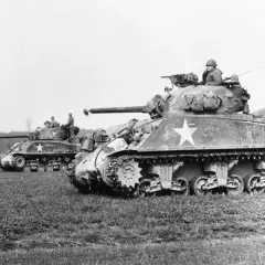 Mehrere Sherman-Panzer, einer mit der Aufschrift "Virgin", stehen auf einem Feld.
