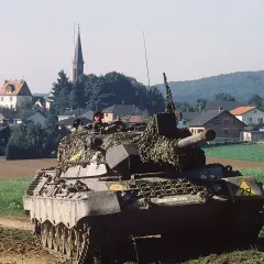 Ein Leopard 1 Panzer mit Tarnnetz fährt durch ein Feld. Die Munition ist bereit für den Einsatz.