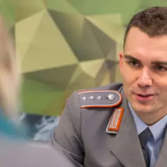 Ein junger Fachoffizier der Bundeswehr im Gespräch, trägt eine graue Uniform mit orangefarbenen Akzenten und Schulterklappen.