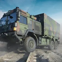 Ein gepanzerter LKW der Bundeswehr mit Tarnmuster fährt über Schienen in einer staubigen Landschaft.