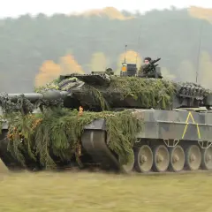 Ein getarnter Panzer Leopard 2 fährt durch herbstliches Gelände. Er sieht aus wie aus einem modernen Weltkrieg.