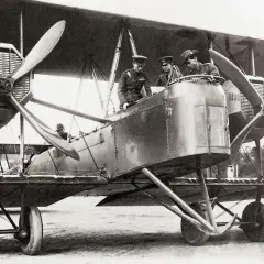 Männer in Uniformen stehen auf einem historischen hochdecker flugzeug.