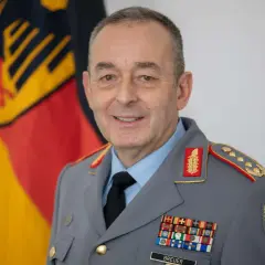 Ein Mann in Uniform mit einem Generalmajor-Abzeichen, vor der deutschen Flagge.