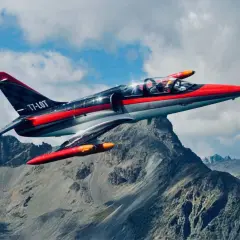 Ein rotes und graues Düsenflugzeug, das wie ein Albatros aussieht, fliegt über felsige Berge.