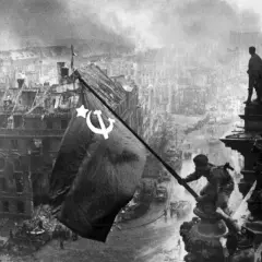 Sowjetische Soldaten hissen die rote Fahne über dem zerstörten Reichstag 1945. Rauch und Trümmer prägen das Bild Berlins.