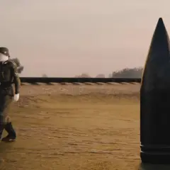 Ein Soldat geht an einer riesigen Kugel vorbei, die schwerer Gustav Munition darstellt. Im Hintergrund ist eine Eisenbahnlinie zu sehen.