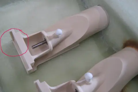 Zwei Teile eines wellenantrieb d-drive Systems, beige, mit Metallachsen und weißen Kugeln, liegen in einer grünen Flüssigkeit.