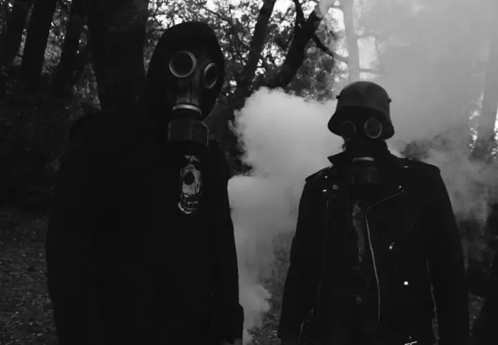 Zwei Personen in Gasmasken, umgeben von Rauch. Der Mann rechts trägt einen Stahlhelm, wie ihn der **Minenwerfer** im Ersten Weltkrieg trug.