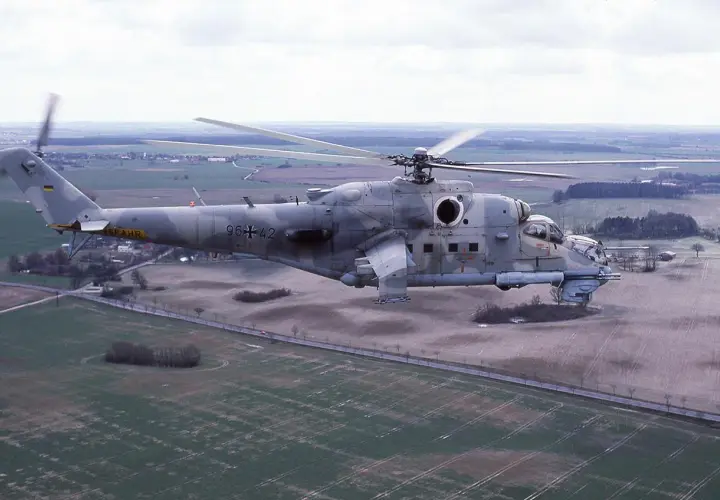 Ein Mi-24 Hind Hubschrauber der Bundeswehr fliegt über ein ländliches Gebiet.
