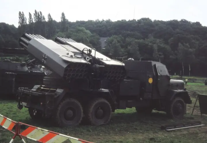Lars Panzer, ein Raketenwerfer auf einem LKW, steht im Gras. Im Hintergrund ein Panzer.