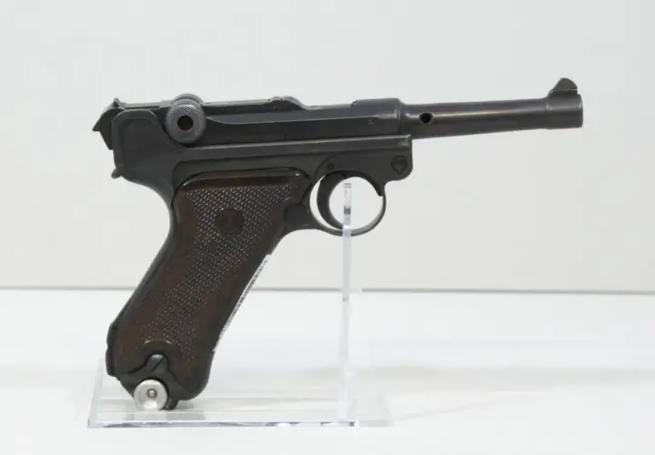 Eine schwarze Luger P08 Wehrmacht Pistole mit braunen Griffschalen, auf einem transparenten Ständer.