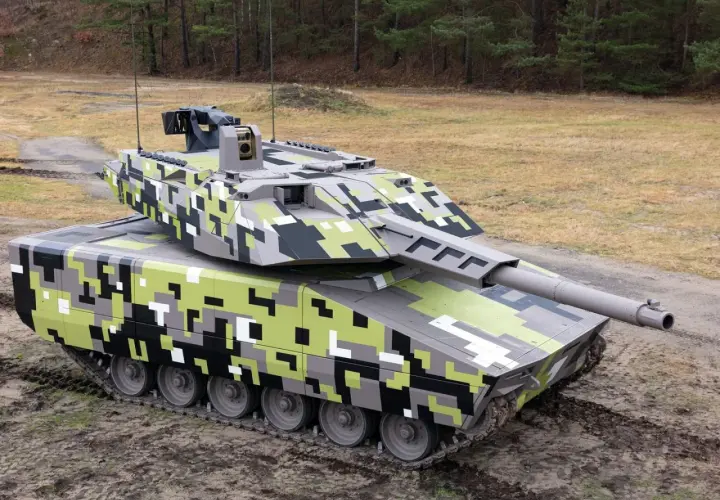 Ein moderner Jagdpanzer mit digitaler Tarnung steht auf schlammigem Untergrund vor einem Wald.