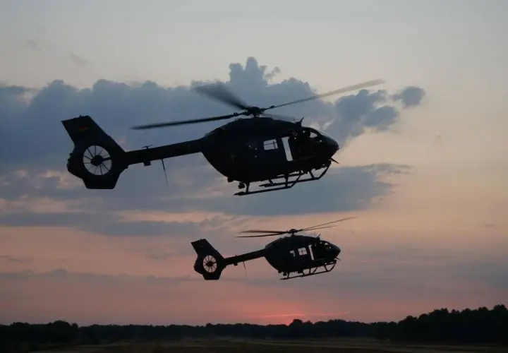 Zwei KSK Hubschrauber fliegen im Abendrot über eine Waldlandschaft.