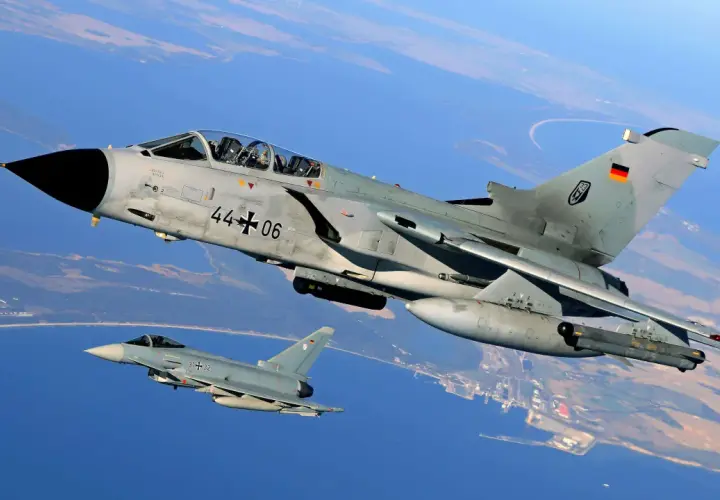 Zwei deutsche Kampfflugzeuge, ein PA-200 Tornado und ein Eurofighter, fliegen über Küstenlandschaft.