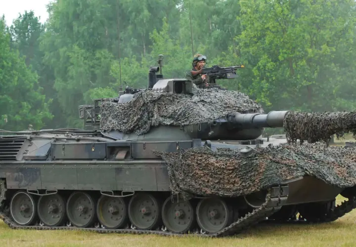 Ein Leopard 1 Panzer mit Tarnnetz und einem Soldaten am Maschinengewehr. Sein Gewicht ist beeindruckend.