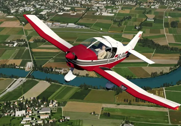 Ein roter und weißer Robin DR 400 fliegt über grüne Felder und einen Fluss.