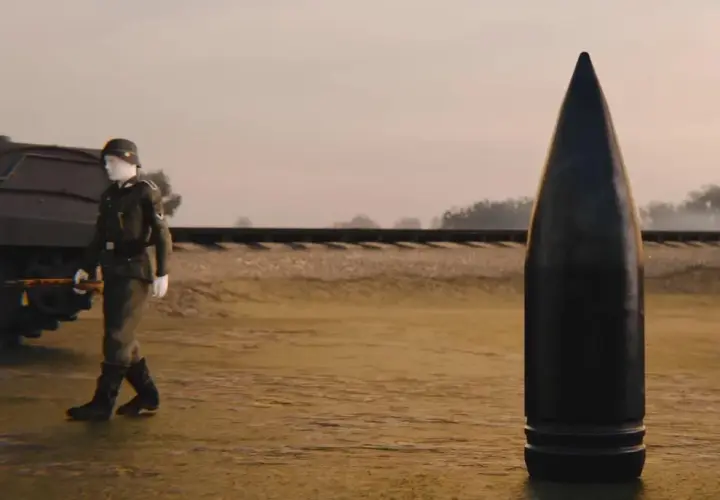 Ein Soldat geht an einer riesigen Kugel vorbei, die schwerer Gustav Munition darstellt. Im Hintergrund ist eine Eisenbahnlinie zu sehen.