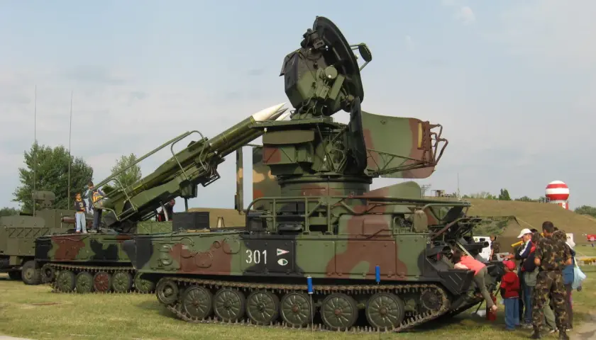 Ein Raketenwerfer SA-6 mit Raketen und Radar steht auf einem Feld. Kinder und Erwachsene betrachten die militärische Ausrüstung.