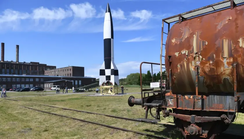 Eine V2-Rakete, ein Symbol deutscher Raketentechnik im 2. Weltkrieg, steht auf einem Freigelände neben einem rostigen Waggon.