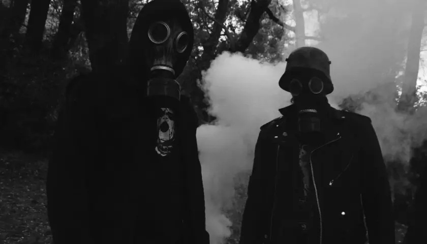 Zwei Personen in Gasmasken, umgeben von Rauch. Der Mann rechts trägt einen Stahlhelm, wie ihn der **Minenwerfer** im Ersten Weltkrieg trug.