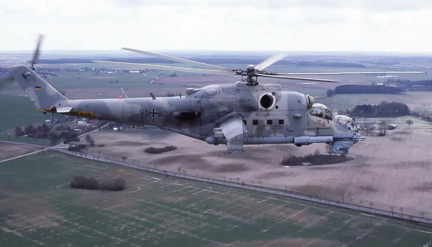 Ein Mi-24 Hind Hubschrauber der Bundeswehr fliegt über ein ländliches Gebiet.
