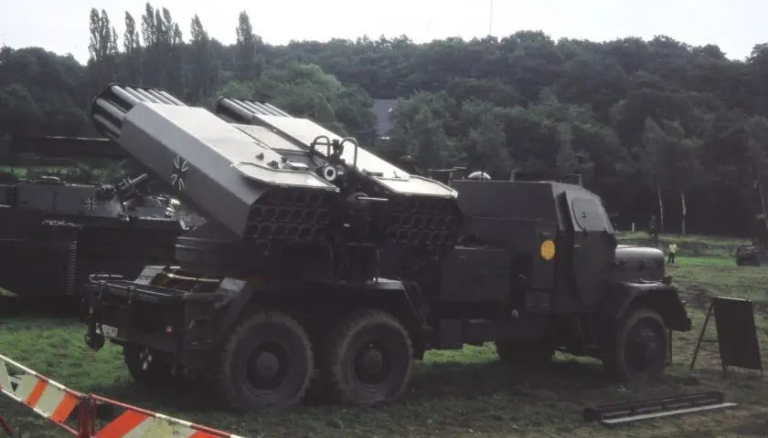 Lars Panzer, ein Raketenwerfer auf einem LKW, steht im Gras. Im Hintergrund ein Panzer.