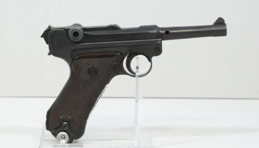 Eine schwarze Luger P08 Wehrmacht Pistole mit braunen Griffschalen, auf einem transparenten Ständer.