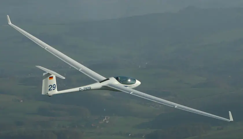 Ein Segelflugzeug, Modell ASG 29, mit der Kennung D-2929, fliegt über eine grüne Landschaft.