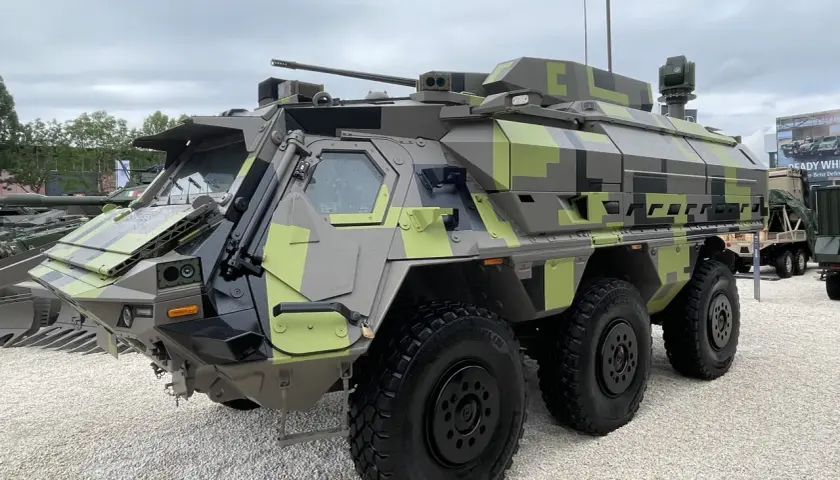 Ein gepanzertes Fahrzeug mit Tarnmuster, das als Fennek-Nachfolger präsentiert wird. Es verfügt über eine Waffenstation und mehrere Sensoren.