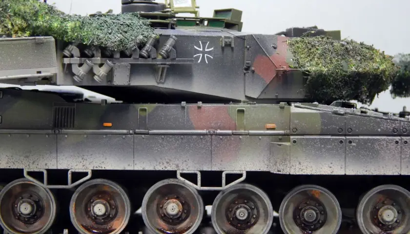 Detailaufnahme eines deutschen Panzers im Tarnmuster mit Tarnnetz. Das Modell zeigt die charakteristischen Räder und Ketten.