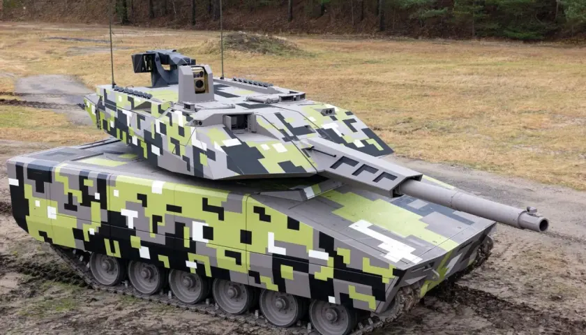 Ein moderner Jagdpanzer mit digitaler Tarnung steht auf schlammigem Untergrund vor einem Wald.