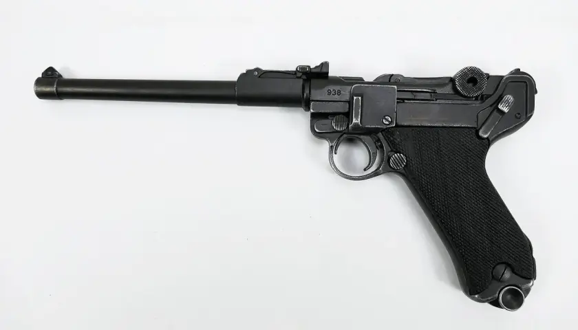 Eine schwarze Luger Pistole mit nummeriertem Schlitten (938) und geriffeltem Griff liegt auf weißem Grund.