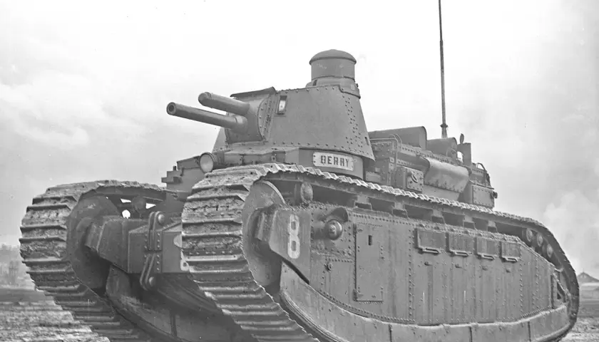 Ein schwerer Panzer, Modell char 2c, mit zwei Kanonen und dem Namen "Berry" auf dem Turm, steht auf schlammigem Gelände.