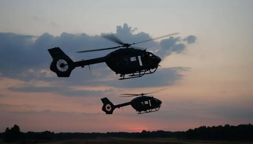 Zwei KSK Hubschrauber fliegen im Abendrot über eine Waldlandschaft.