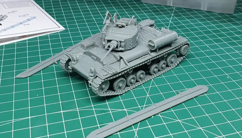 Ein grauer Modellbausatz eines Valentine Panzers liegt auf einer grünen Schneidematte. Zwei separate Panzerplatten liegen daneben.
