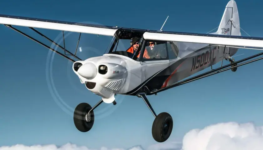 Zwei Piloten fliegen in einer CubCrafters X-Cub über den Wolken.