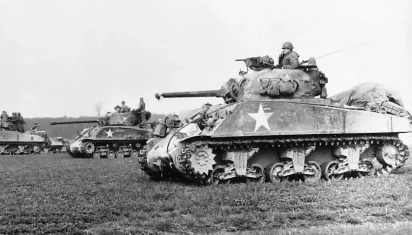Mehrere Sherman-Panzer, einer mit der Aufschrift "Virgin", stehen auf einem Feld.