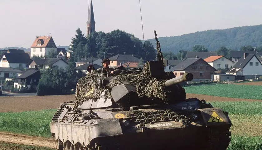 Ein Leopard 1 Panzer mit Tarnnetz fährt durch ein Feld. Die Munition ist bereit für den Einsatz.
