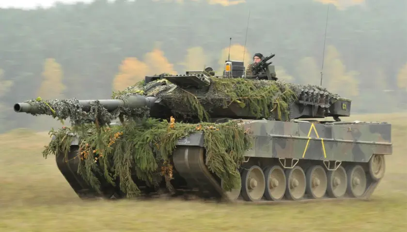 Ein getarnter Panzer Leopard 2 fährt durch herbstliches Gelände. Er sieht aus wie aus einem modernen Weltkrieg.