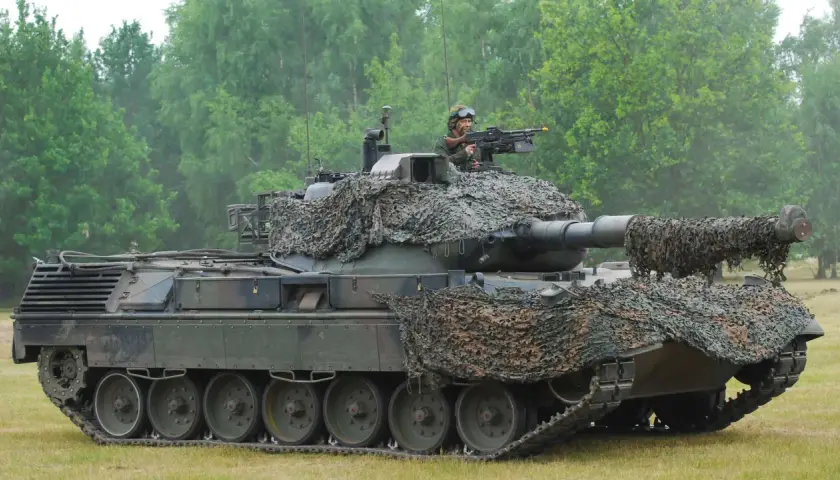Ein Leopard 1 Panzer mit Tarnnetz und einem Soldaten am Maschinengewehr. Sein Gewicht ist beeindruckend.