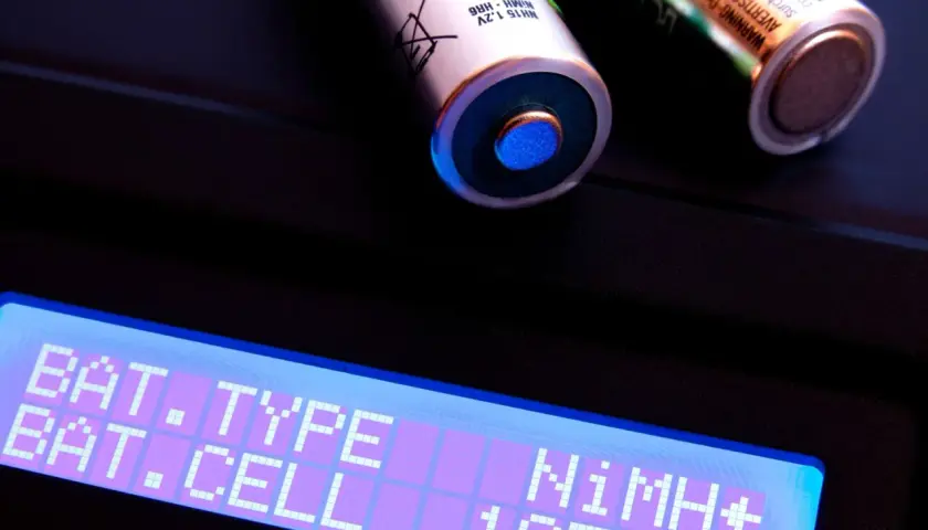 NiMH Akku lagern: Ein Ladegerät zeigt "NiMH+ 1CELL" an, daneben liegen zwei NiMH-Akkus.