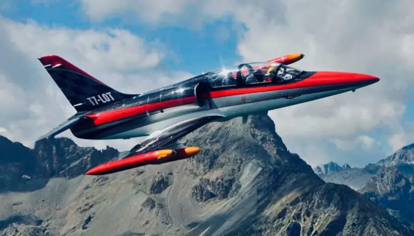 Ein rotes und graues Düsenflugzeug, das wie ein Albatros aussieht, fliegt über felsige Berge.